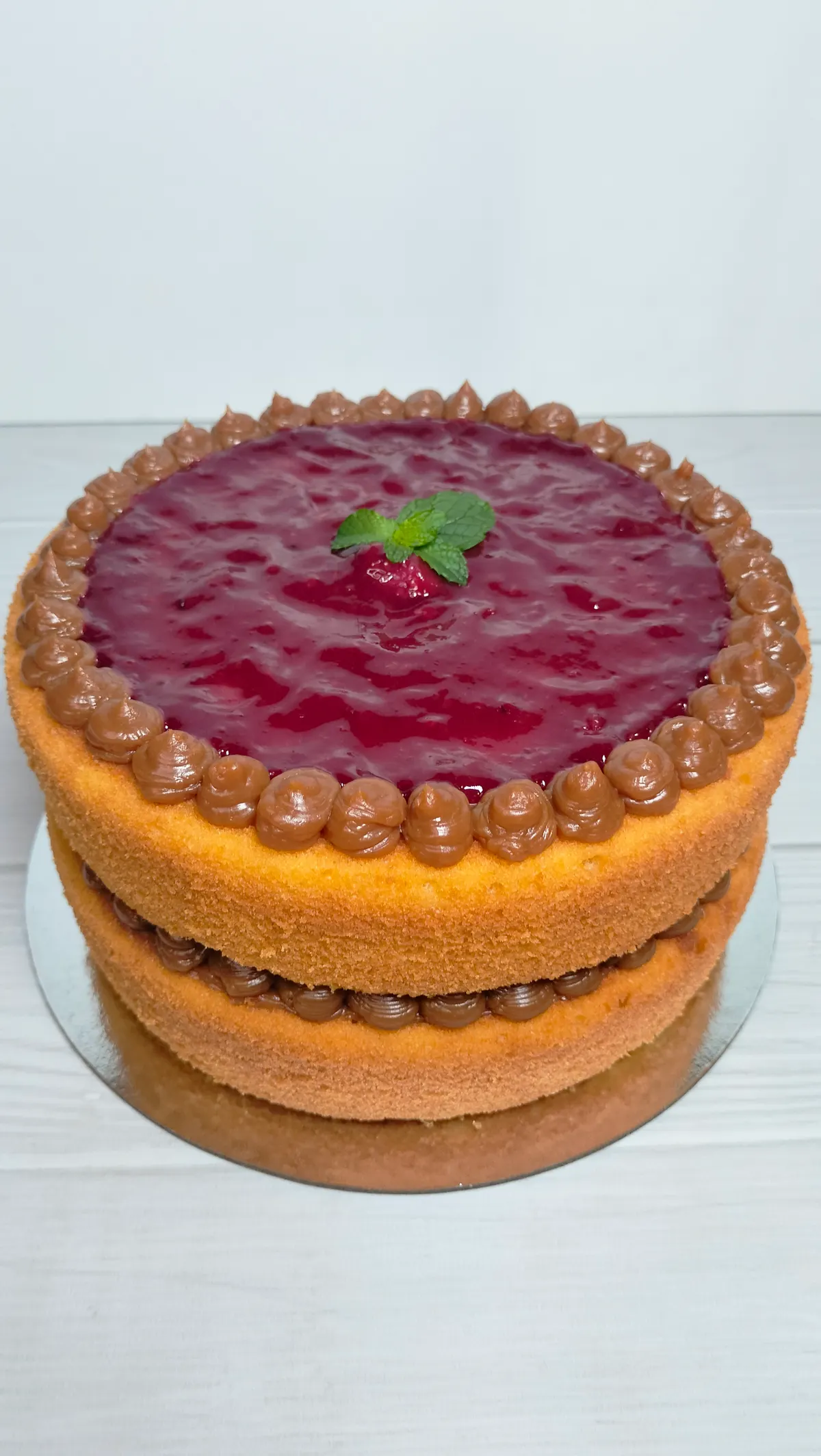 Torta de dos capas con cobertura de frutos rojos, borde de crema y una hoja de menta