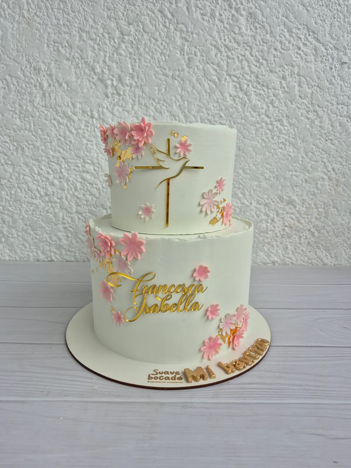 Torta de bautizo de dos pisos con flores rosadas, una cruz dorada y el nombre Francesca Isabella