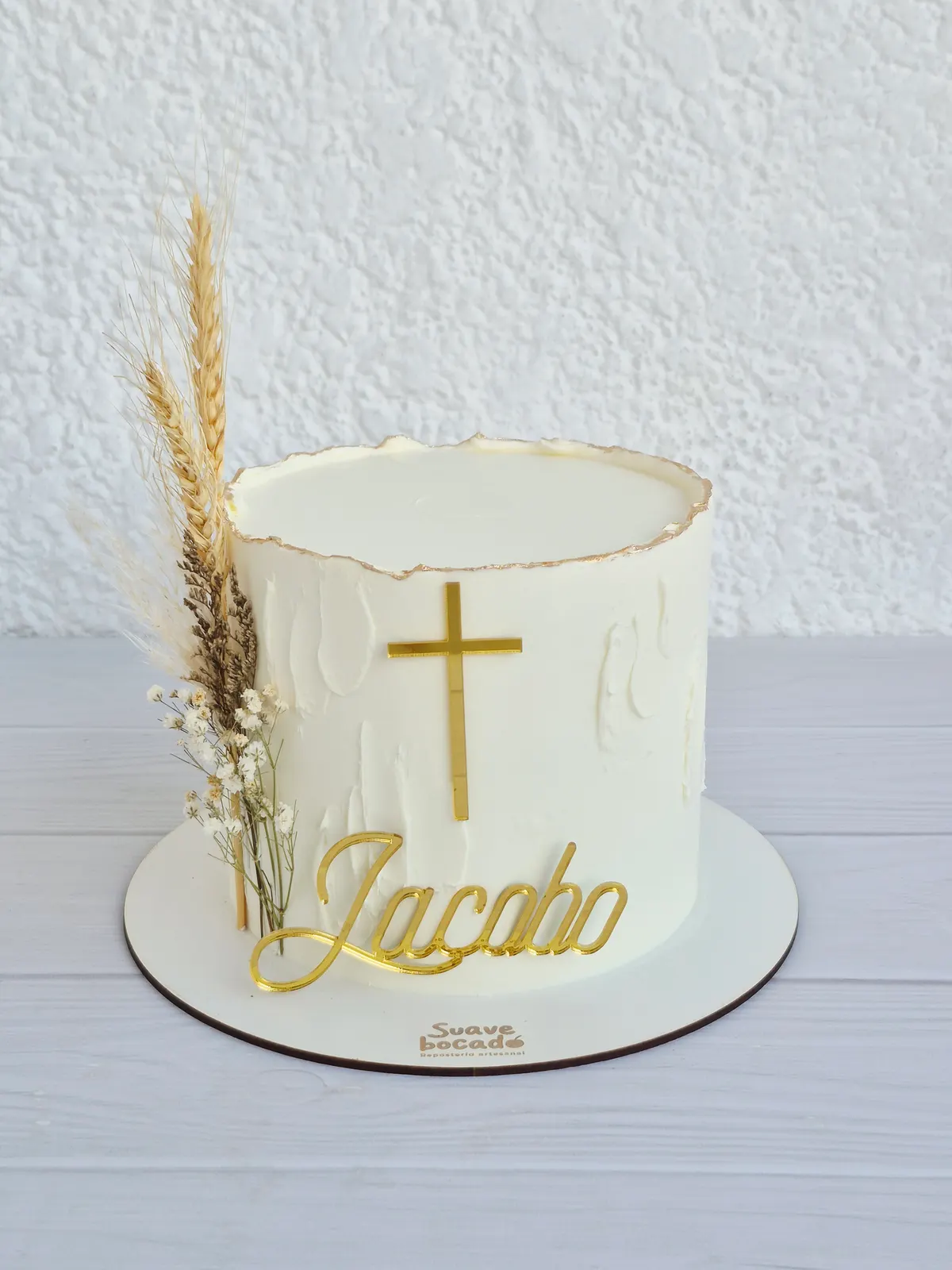 Torta de bautizo blanca con una cruz dorada, espigas secas y el nombre Jacobo