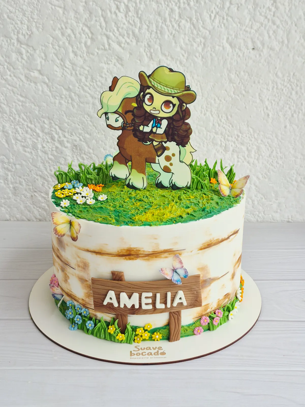 Torta de granja con pasto de crema, flores, una vaquera ilustrada y un letrero con el nombre Amelia