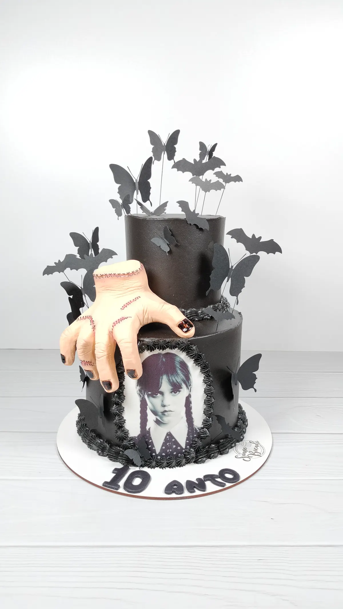 Torta de Halloween de dos pisos en negro con murciélagos, la mano Dedos y una imagen de Merlina