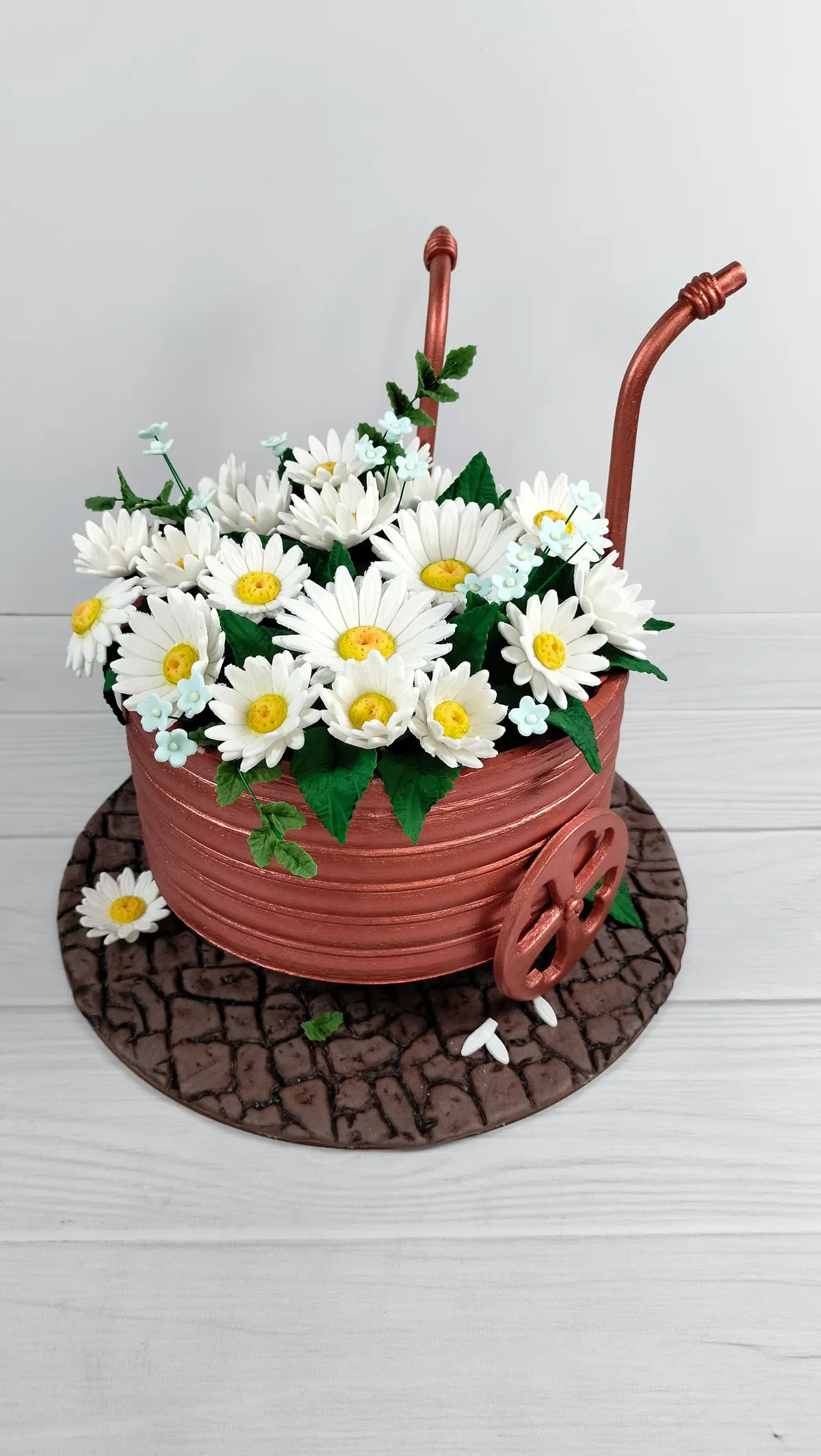 Torta en forma de carretilla con margaritas blancas sobre un camino de piedras